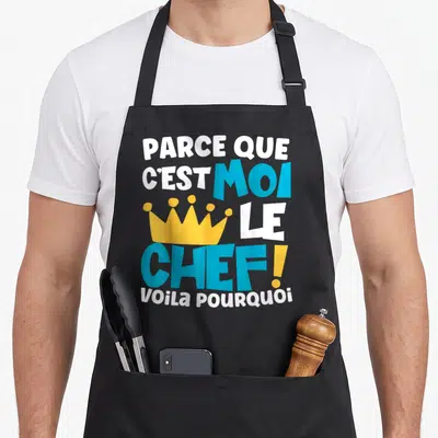 Tablier de cuisine noir avec inscription blanche et bleue et une couronne jaune stylisée au centre du motif imprimé.