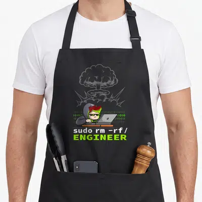 Tablier de cuisine noir avec illustration d'un codeur aux cheveux verts devant un laptop et une explosion en arrière-plan.