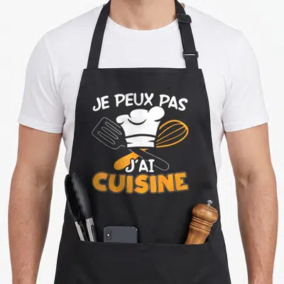 Tablier de cuisine noir avec toque, spatule et fouet orange portant l'inscription Je peux pas j'ai cuisine.