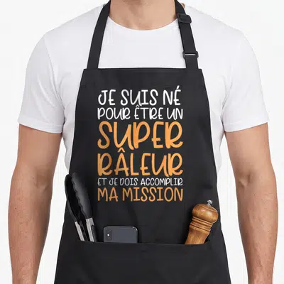 Tablier de cuisine noir avec inscription blanche et orange disant Je suis né pour être un super râleur et je dois accomplir ma mission.