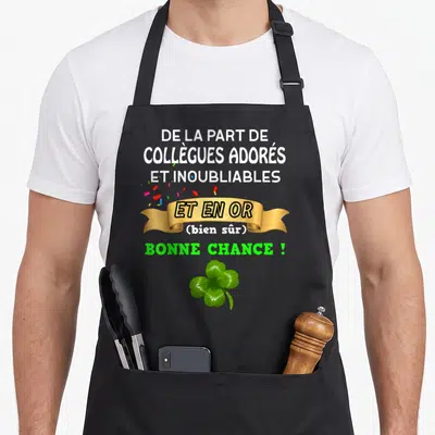 Tablier de cuisine noir avec bannière dorée, confettis colorés et trèfle à quatre feuilles vert sur fond uni.