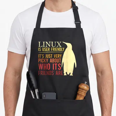 Tablier de cuisine noir avec illustration de pingouin jaune et texte coloré sur fond uni.