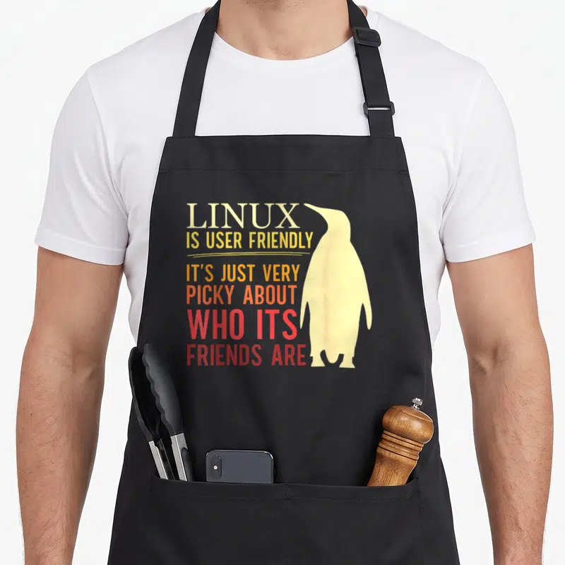 Tablier de cuisine noir avec illustration de pingouin jaune et texte coloré sur fond uni.