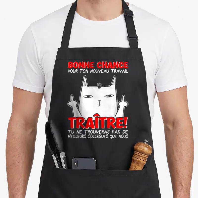 Tablier de cuisine noir avec un chat blanc levant les deux doigts et le texte Bonne chance Traître en rouge.