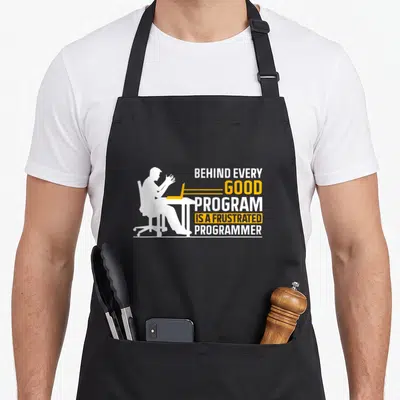 Tablier de cuisine noir avec silhouette blanche d'un homme au bureau et texte humoristique en blanc et orange.