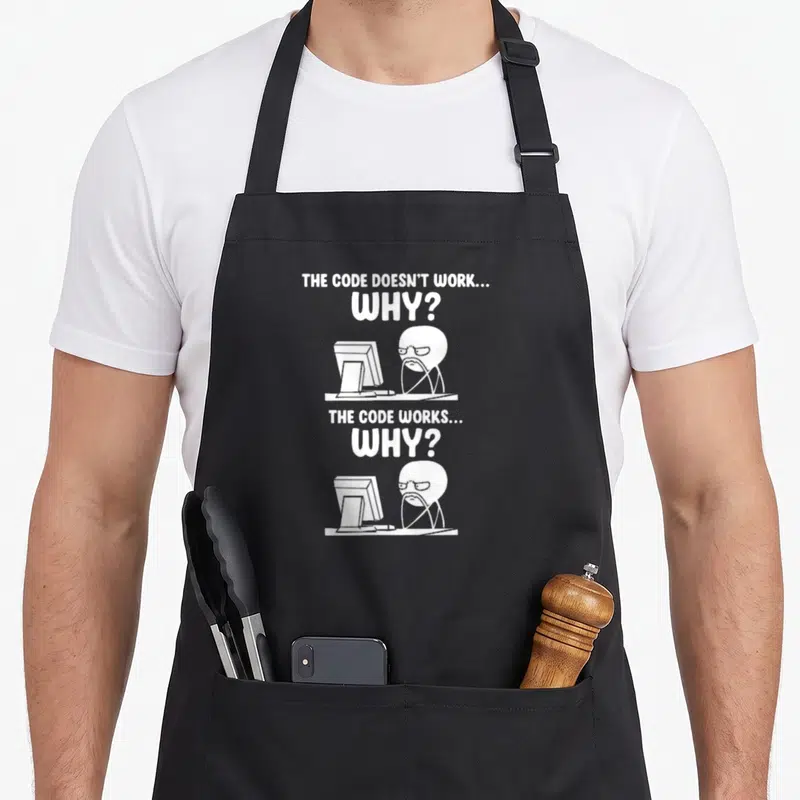 Tablier de cuisine noir avec illustration blanche d'un personnage au bureau devant un écran et le texte THE CODE DOESN'T WORK WHY.