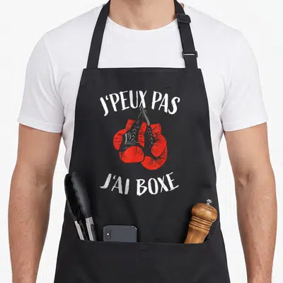 Tablier de cuisine noir avec deux gants de boxe rouges suspendus et le texte blanc J'peux pas j'ai boxe