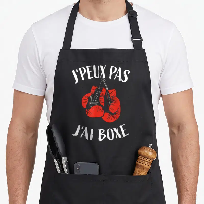 Tablier de cuisine noir avec deux gants de boxe rouges suspendus et le texte blanc J'peux pas j'ai boxe