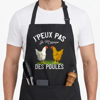 Tablier de cuisine noir avec inscription j'peux pas et illustration de deux poules blanche et jaune sur un bout de verdure.