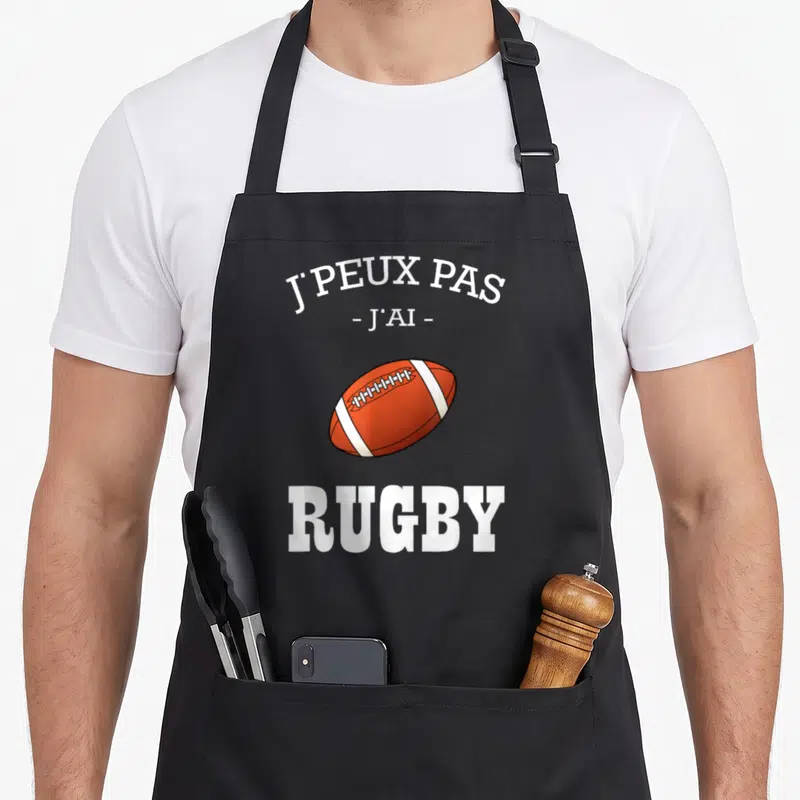 Tablier de cuisine noir avec un ballon de rugby orange et le texte blanc J'peux pas j'ai rugby