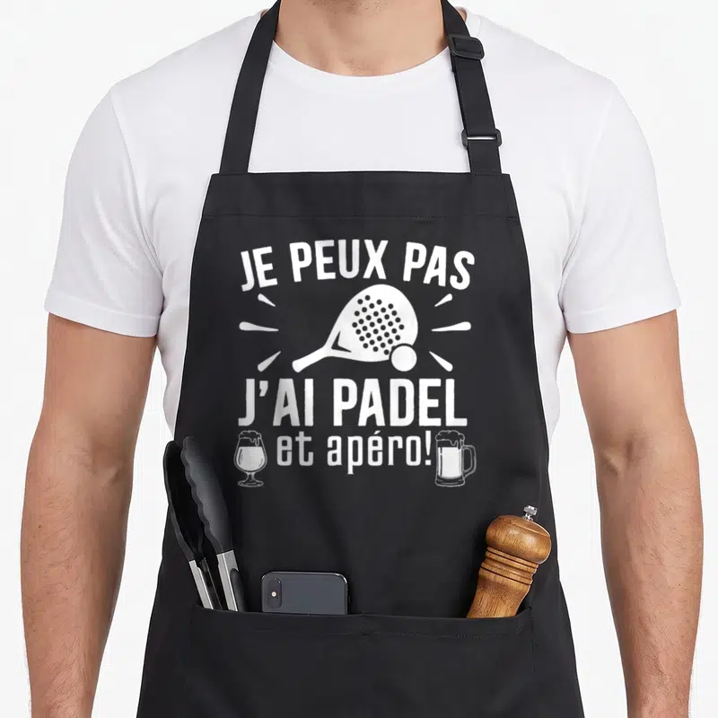Tablier de cuisine noir avec inscription je peux pas j'ai padel et apéro illustrée d'une raquette et de deux verres.