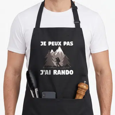 Tablier de cuisine noir avec silhouette de randonneur et texte Je peux pas j'ai rando sur fond de montagnes.
