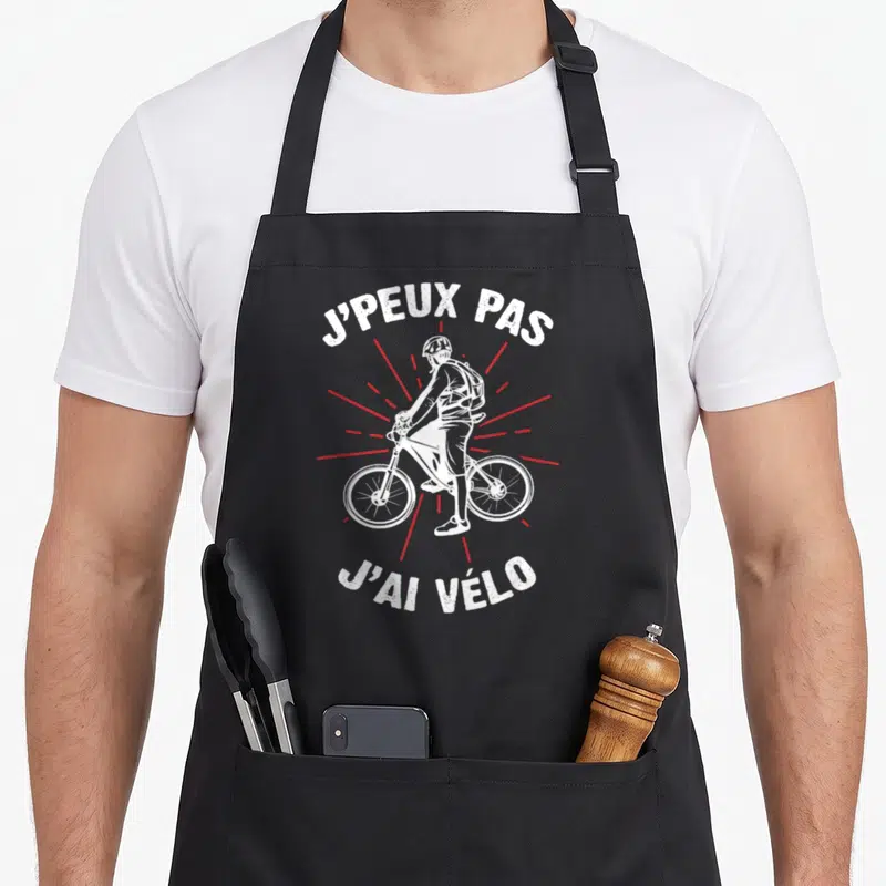Tablier de cuisine noir avec illustration cycliste blanche, casque, sac à dos et texte j'ai vélo sur fond gris uni.