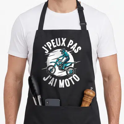 Tablier de cuisine noir avec illustration d'un pilote de moto enduro et le texte j'peux pas j'ai moto en blanc.