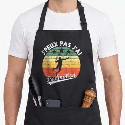 Tablier de cuisine noir avec motif circulaire vintage montrant un joueur de badminton et le texte jpeux pas jai badminton.
