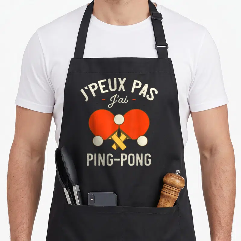 Tablier de cuisine noir avec deux paddles rouges croisés et texte blanc J'peux pas j'ai ping-pong
