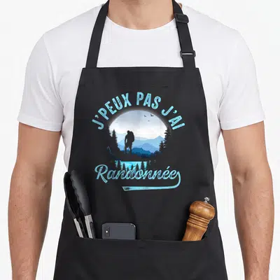 Tablier de cuisine noir avec illustration d'un randonneur face à des montagnes et le texte J'peux pas j'ai randonnée imprimé en bleu clair.