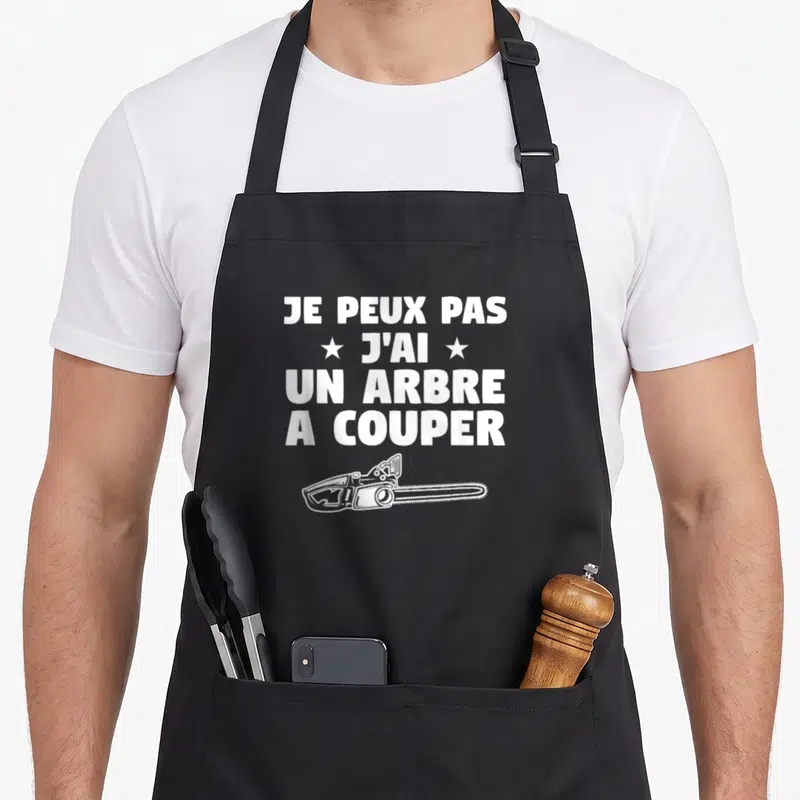 Tablier de cuisine noir avec texte blanc je peux pas j'ai un arbre a couper et illustration de scie à moteur.