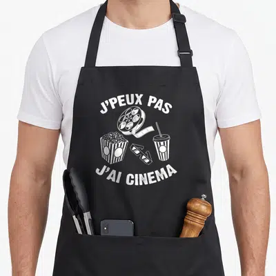 Tablier de cuisine noir avec inscription j'peux pas j'ai cinéma et illustrations de popcorns, bobine et gobelet.