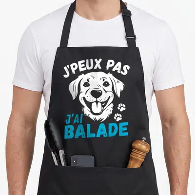 Tablier de cuisine noir avec tête de chien souriant et texte j'peux pas j'ai balade en blanc et bleu.