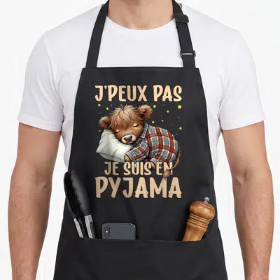 Tablier de cuisine noir avec une vache highland dormant en chemise à carreaux et texte humoristique beige.