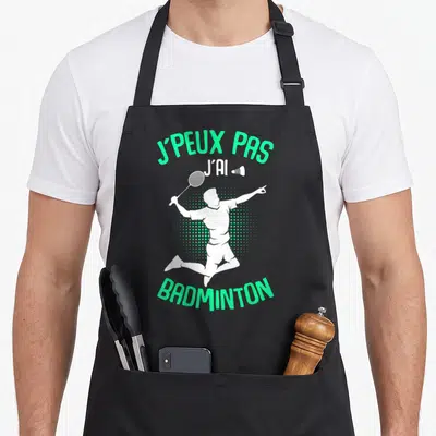 Tablier de cuisine noir avec silhouette blanche de joueur de badminton en saut et texte vert j'peux pas j'ai badminton homme enfant