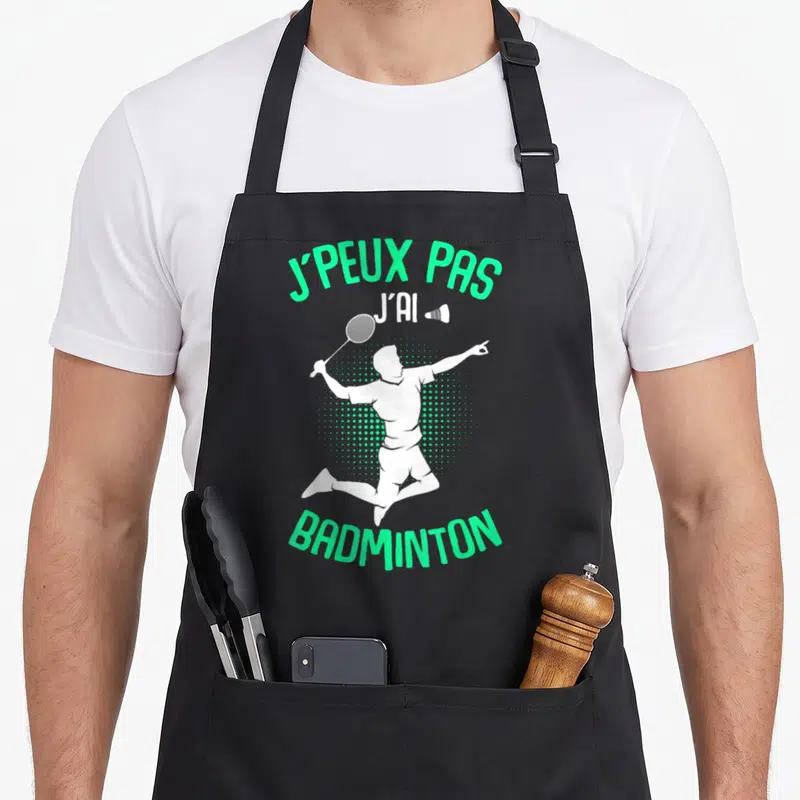 Tablier de cuisine noir avec silhouette blanche de joueur de badminton en saut et texte vert j'peux pas j'ai badminton homme enfant
