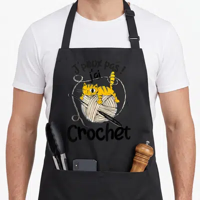 Tablier de cuisine noir avec illustration d'un chat orange sur un ballotin de laine et une aiguille à crochet.