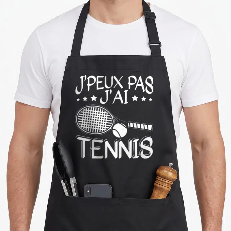 Tablier de cuisine noir avec inscription j'peux pas j'ai tennis et une raquette blanche.
