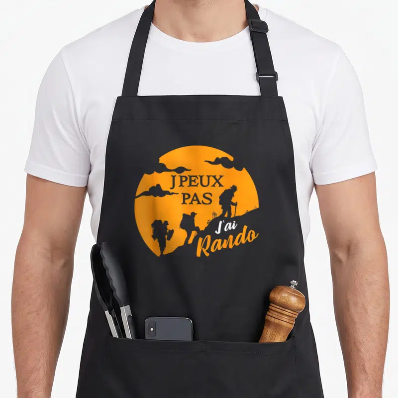 Tablier de cuisine noir avec motif circulaire orange représentant des silhouettes de randonneurs et le texte J peux pas j ai rando.