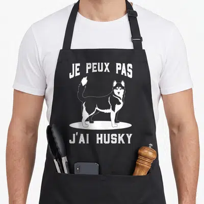 Tablier de cuisine noir avec illustration blanche d'un husky et le texte je peux pas j'ai husky imprimé en haut et en bas.
