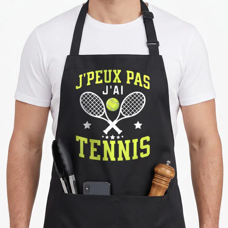 Tablier de cuisine noir avec deux raquettes de tennis blanches croisées et une balle jaune au centre du motif imprimé.