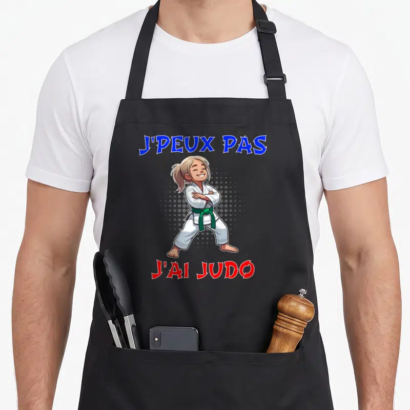 Tablier de cuisine noir avec une illustration de jeune fille en judo et ceinture verte, texte J'peux pas J'ai Judo.