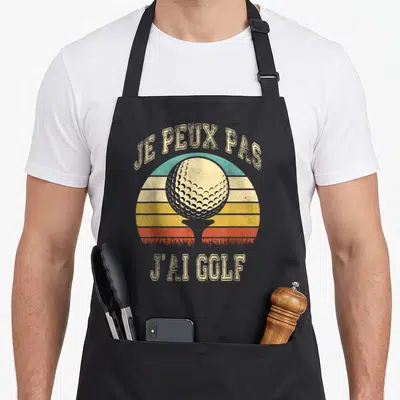 Tablier de cuisine noir avec une balle de golf sur fond de soleil rétro et le texte je peux pas j'ai golf.