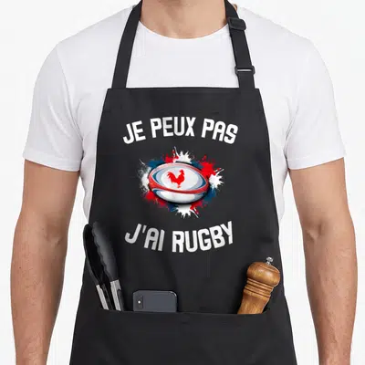 Tablier de cuisine noir avec motif ballon de rugby tricolore et coq gaulois au centre des éclaboussures.