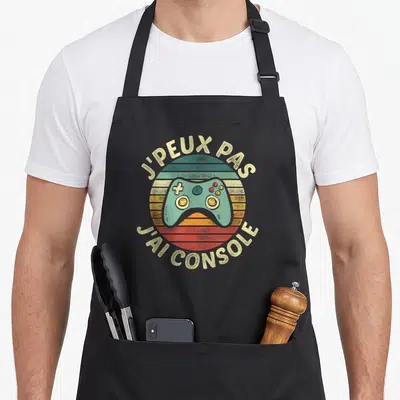 Tablier de cuisine noir avec illustration manette de jeu vidéo et texte j'peux pas j'ai console en style rétro.