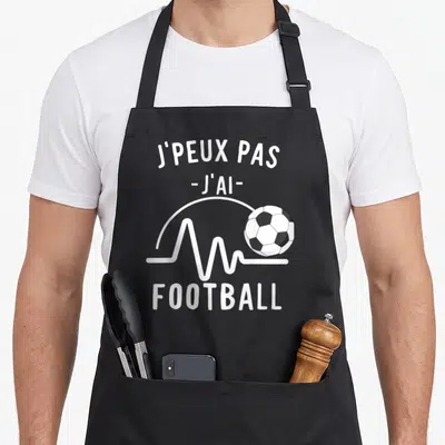 Tablier de cuisine noir avec inscription j'peux pas j'ai football et ballon de soccer blanc sur fond gris uni.