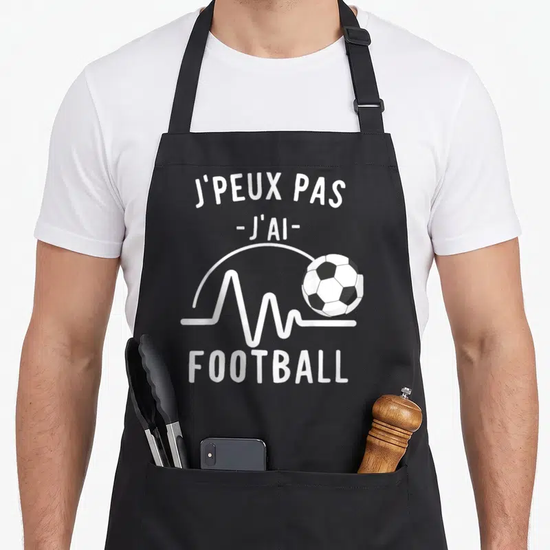 Tablier de cuisine noir avec inscription j'peux pas j'ai football et ballon de soccer blanc sur fond gris uni.