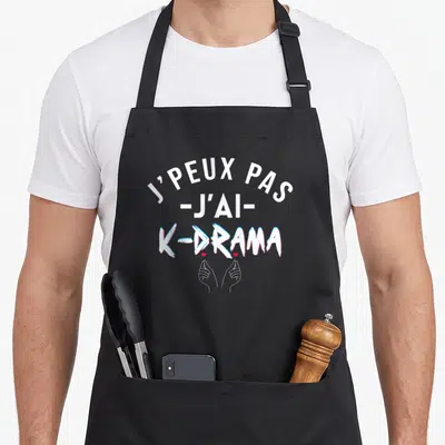 Tablier de cuisine noir avec l'inscription J'peux pas j'ai K-drama et deux mains formant un petit cœur rouge.