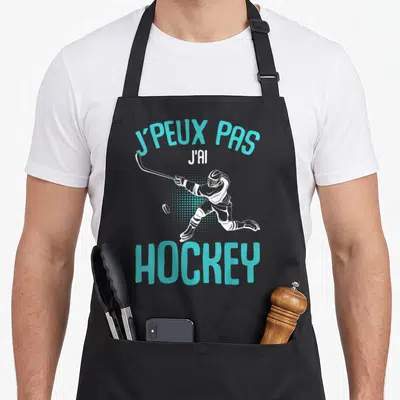 Tablier de cuisine noir avec illustration d'un joueur de hockey et le texte J'peux pas j'ai hockey en turquoise.