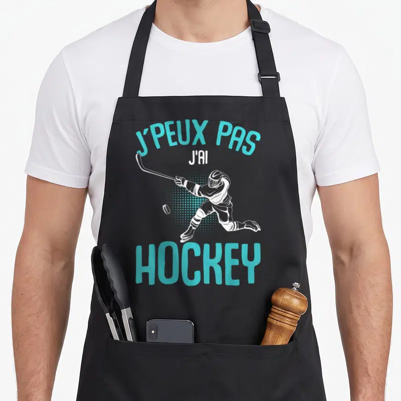 Tablier de cuisine noir avec illustration d'un joueur de hockey et le texte J'peux pas j'ai hockey en turquoise.