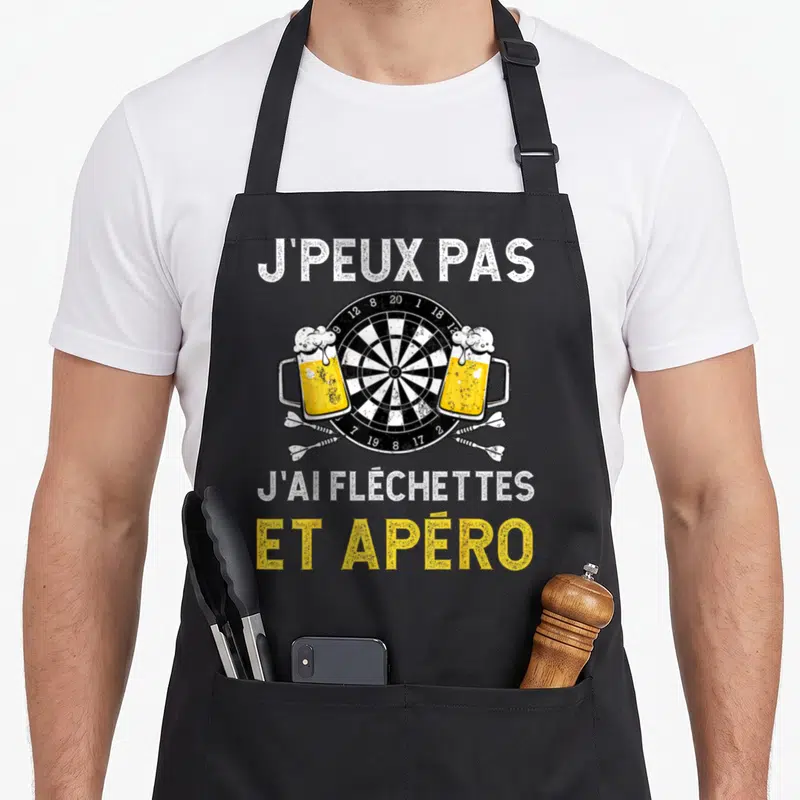 Tablier de cuisine noir avec cible de fléchettes, deux verres de bière et texte humoristique blanc et jaune.
