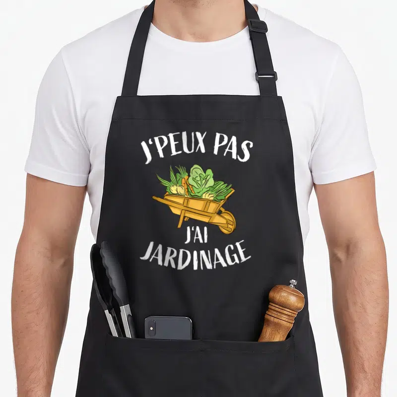 Tablier de cuisine noir avec une illustration de brouette en bois remplie de légumes frais et verts.