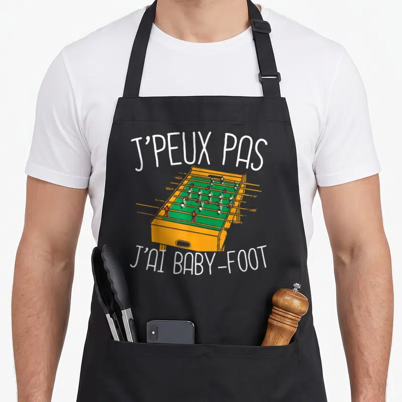 Tablier de cuisine noir avec illustration de baby-foot orange et texte blanc J'peux pas j'ai baby-foot