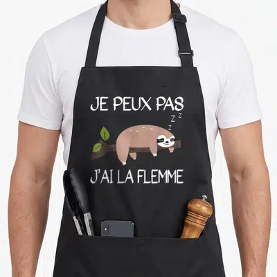 Tablier de cuisine noir avec un fourmi paresseux dormant sur une branche et le texte je peux pas j'ai la flemme imprimé en blanc.