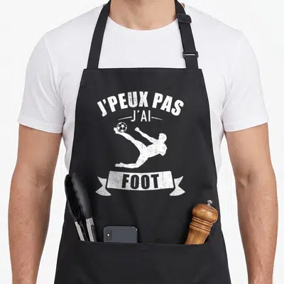 Tablier de cuisine noir avec inscription j'peux pas j'ai foot et silhouette de joueur de football en action.