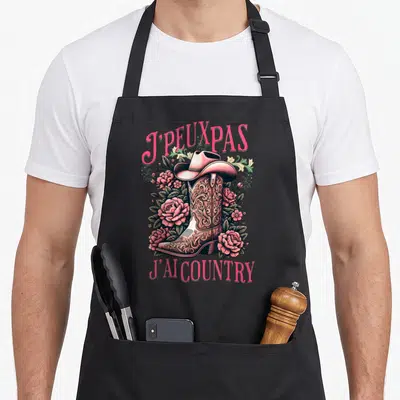 Tablier de cuisine noir avec une botte rose ornée de motifs et des fleurs roses autour du texte J'peux pas j'ai country.