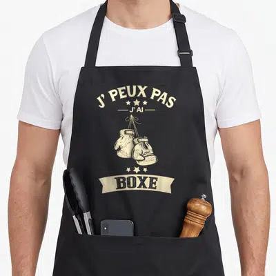 Tablier de cuisine noir avec l'inscription j'peux pas j'ai boxe et deux gants de boxing suspendus par des cordes.
