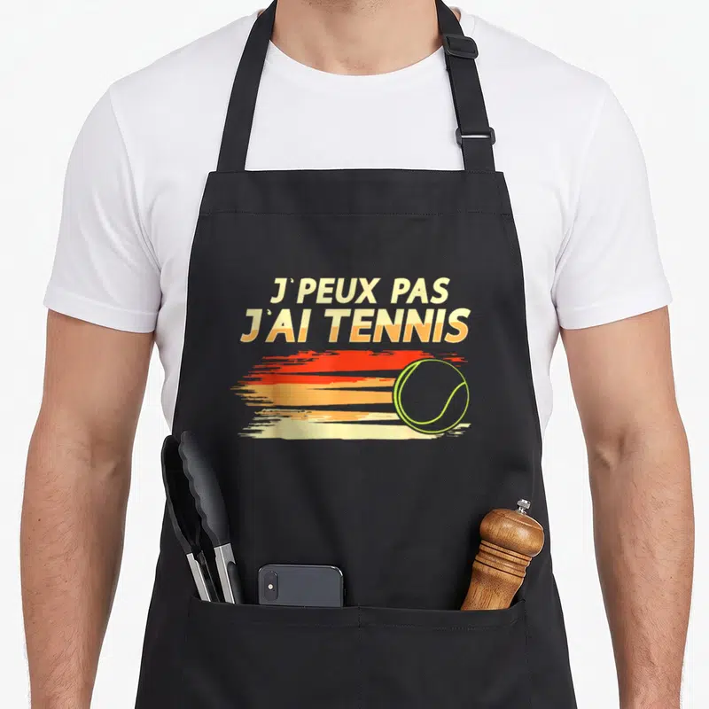 Tablier de cuisine noir avec inscription j peux pas j ai tennis et illustration de balle de tennis sur fond de soleil orange