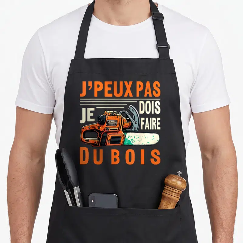 Tablier de cuisine noir avec une tronçonneuse orange et le texte J'peux pas je dois faire du bois imprimé en orange et blanc.